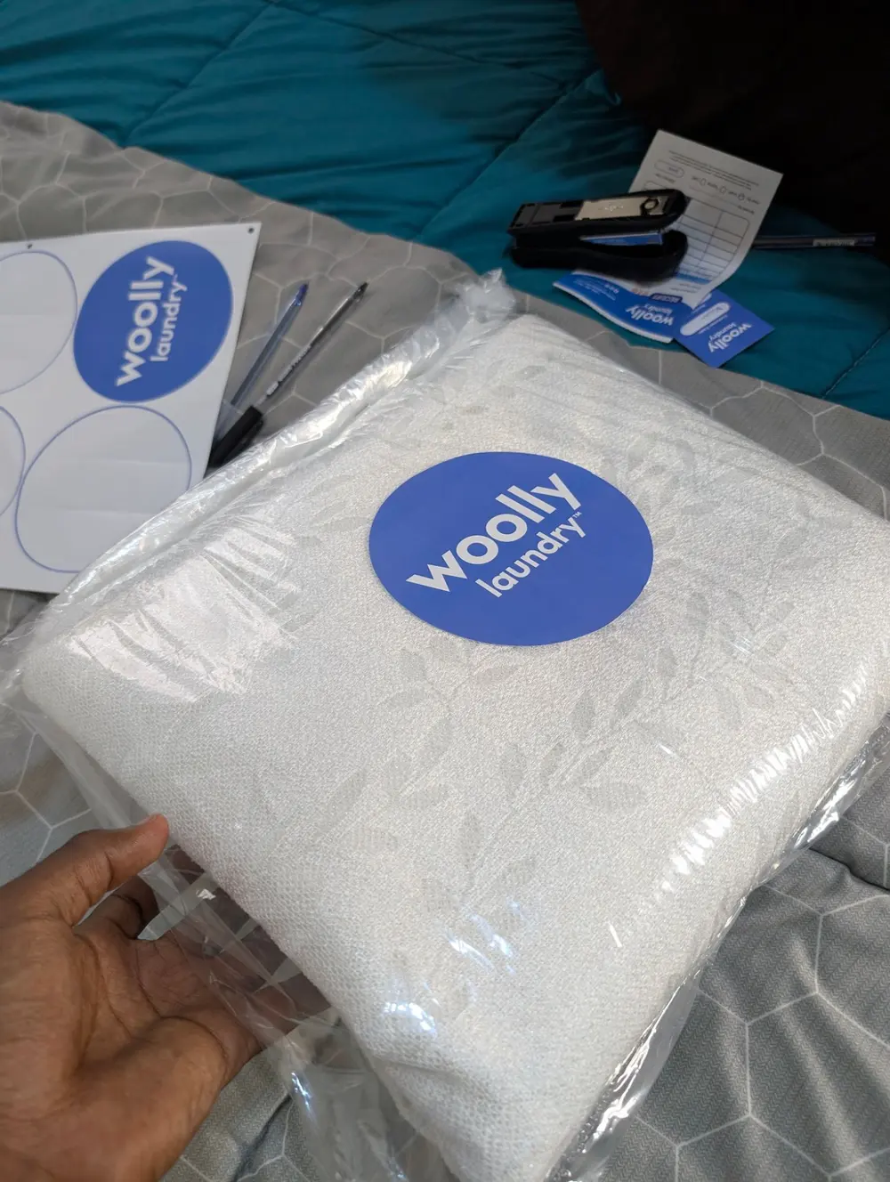 A folded white blanket packed in clear plastic and sealed with a round blue Woolly Laundry sticker