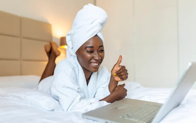 Happy guest in a white bathrobe and towel relaxing on a fresh white bed